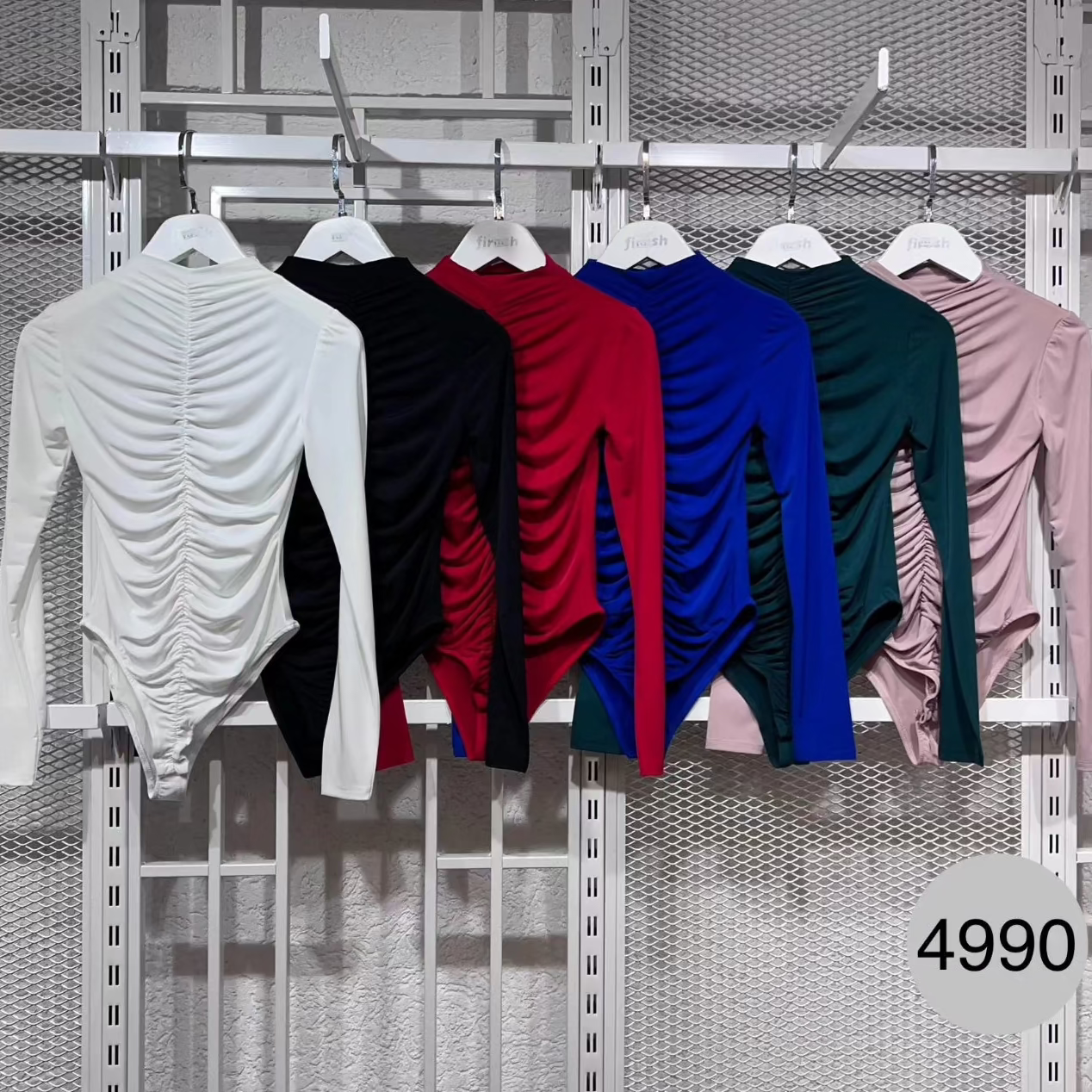 Colorful long-sleeve bodysuits on hangers against a metallic grid background.